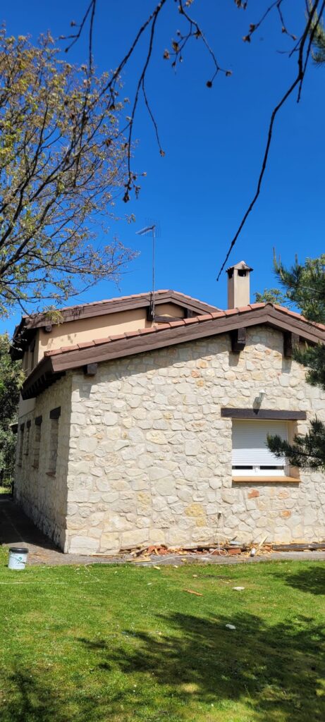 Casa de piedra con techo inclinado en proceso de arreglo de aleros, mejorando la durabilidad y la protección contra el clima