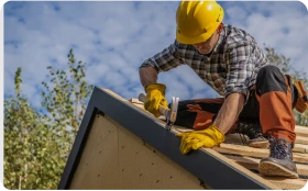 Construcción de Tejados y Cubiertas 1 Tejados Alcala Henares Trabajador con casco y herramientas realizando construcción de tejados y cubiertas, mejorando la estructura de un techo bajo el cielo azul
