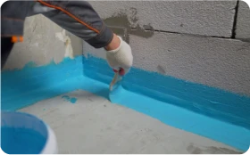 Rehabilitación de fachadas 6 Tejados Alcala Henares Aplicación de revestimiento impermeabilizante en la base de un muro durante la rehabilitación de fachadas para mejorar la protección contra la humedad